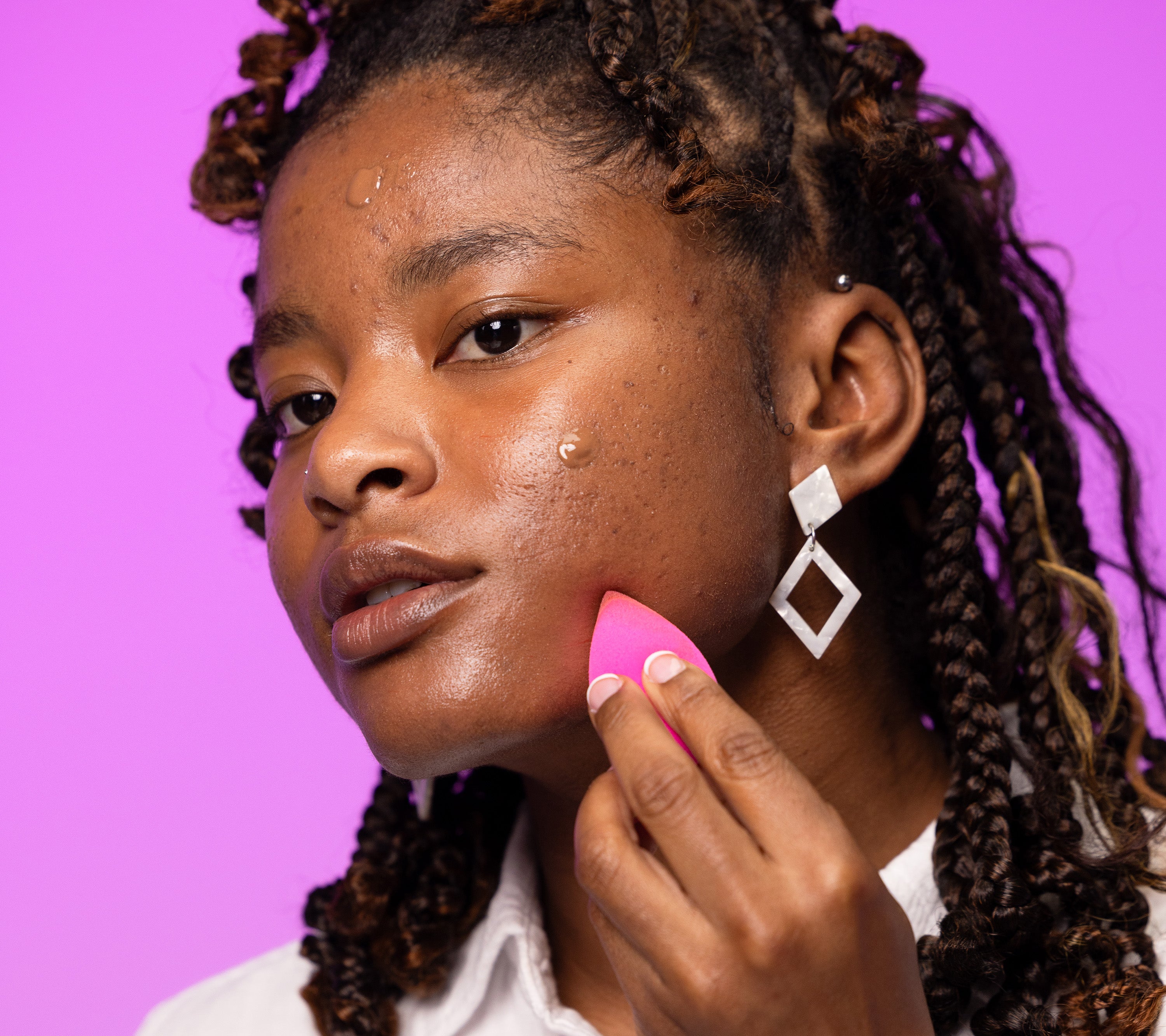 a woman using a beautyblender sponge to apply the boldhue foundation to her skin