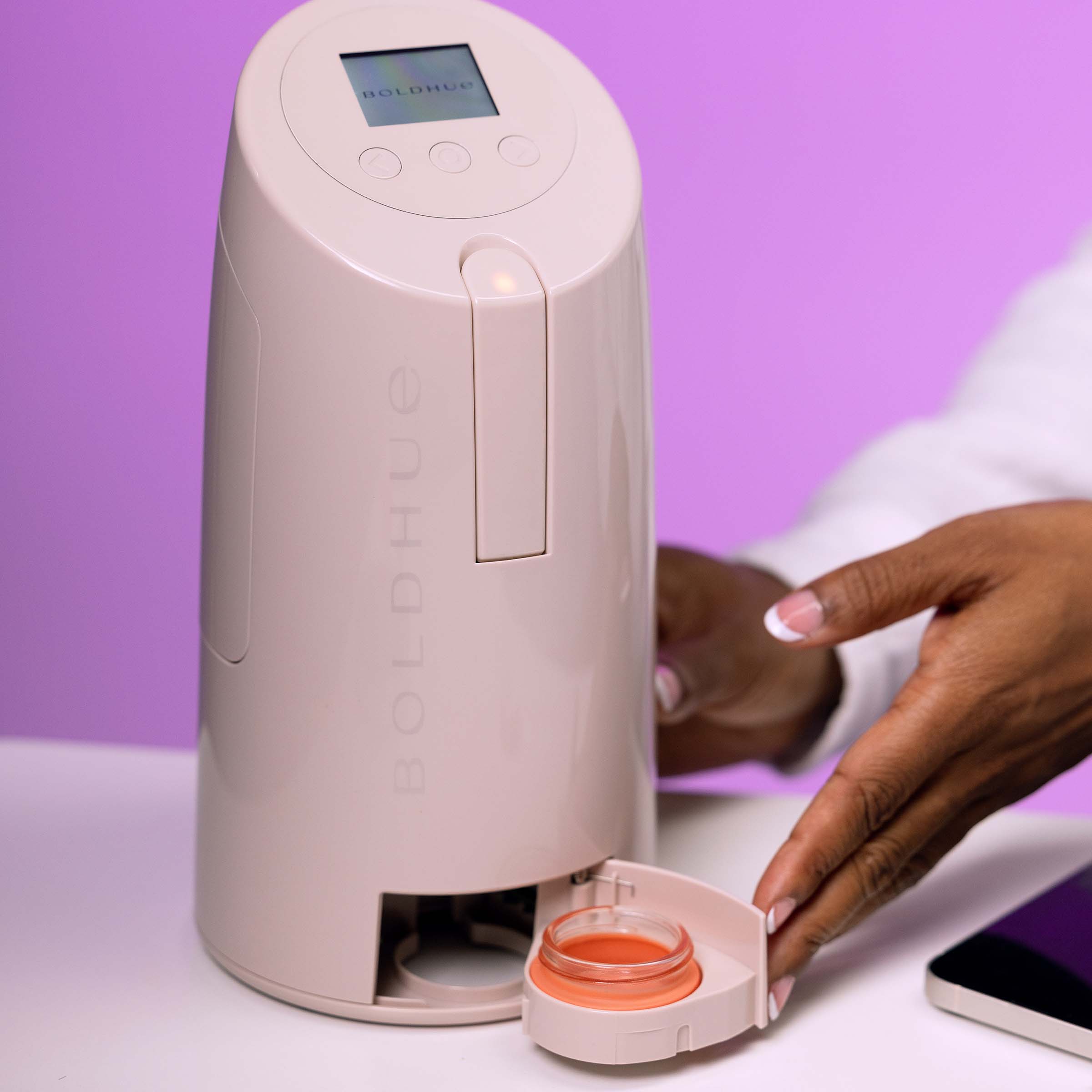 a picture of the boldhue device with the drawer open and a jar sitting inside with a model pushing the door closed to start mixing her custom foundation